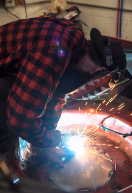 A welder in action, with sparks flying while performing a MIG weld on a vehicle's body panel.
