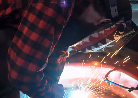 A welder in action with sparks flying during body panel repair work.