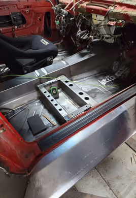 The interior of a red project car featuring extensive custom metalwork, including new floor pans, transmission tunnel, and a seat mounting bracket.