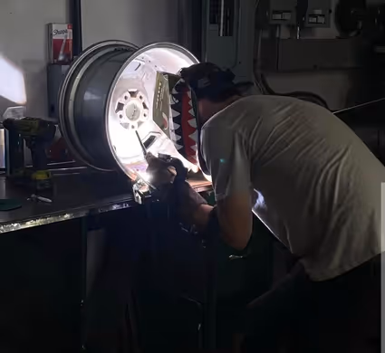 A skilled technician performing a precise TIG weld on the inside of a custom aluminum wheel.