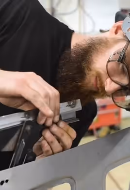 A close-up of a fabricator wearing a custom-painted welding helmet while working on the intricate details of a car door assembly.
