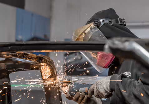 Cutting into a car body panel with sparks flying during fabrication.