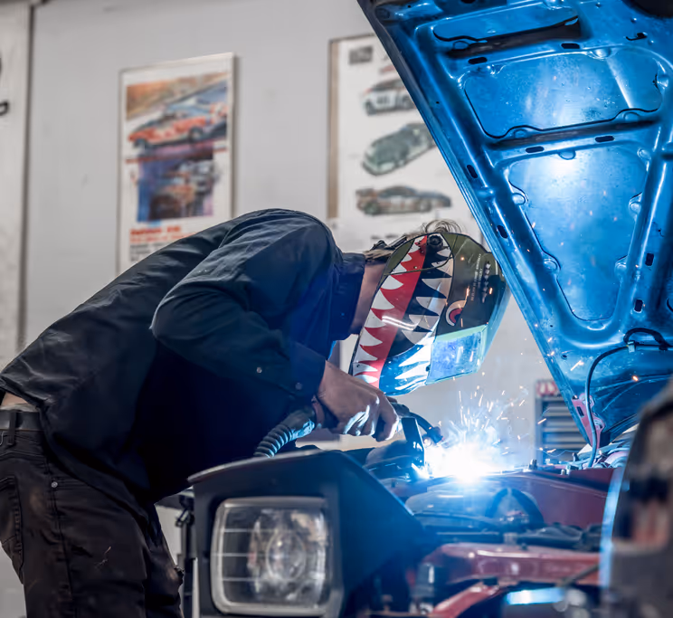 Dan performing a precise weld with blue arc light in the shop.