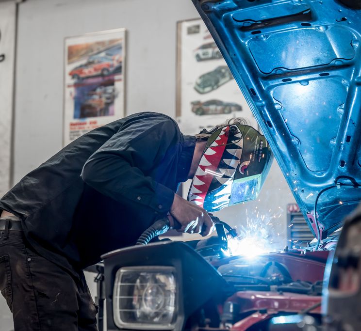 Dan performing a precise weld with blue arc light in the shop.