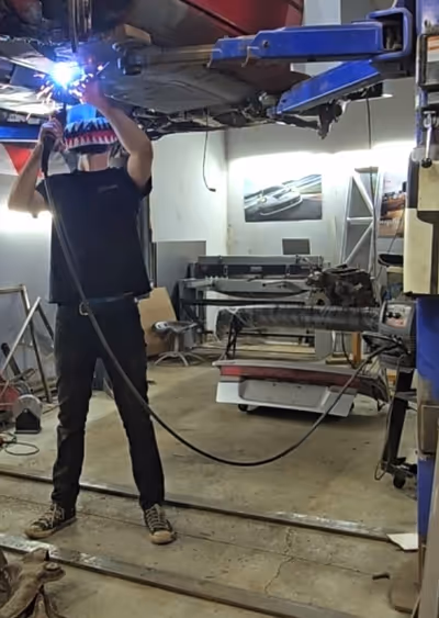 A close-up of a fabricator wearing a custom-painted welding helmet while working on the intricate details of a car door assembly.