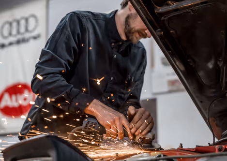 Grinding and prep work around the front of a red car engine bay during fabrication.